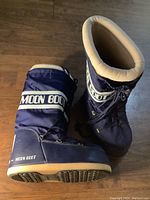 Top-down and side view of navy blue Moon Boots showing branding, laces, and sole detail.