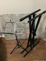 Photo showing silver music sheet stand and black keyboard stand placed together on wooden floor.