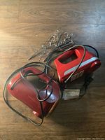 Two red hand mixers laid on wooden surface with metal beaters and dough hooks attached or nearby, cords visible.