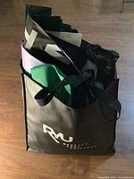 Photo showing a black reusable tote bag with RAU branding filled with various folded reusable bags in different colors including green and purple.