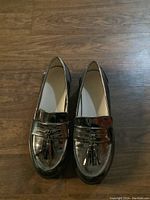 Top-down view of the pair of silver metallic tassel loafers on wooden floor.