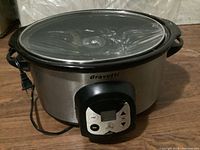 Full view of the Bravetti slow cooker showing stainless steel exterior, glass lid, and black handles.