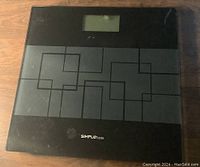 Top view of the Simplus smart scale powered off showing black glass surface with geometric line pattern and logo near bottom.