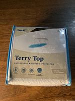Front view of the Lucid Terry Top waterproof mattress protector packaging showing brand, product name, features and warranty information.