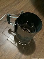 Top down angled view of the metal charcoal chimney starter showing handle and cylindrical vented body.