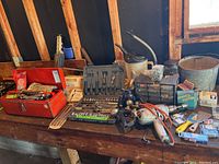 Overview of the wooden workbench with a variety of hand tools, socket sets, Black & Decker corded drill, metal greaser, and small containers with screws.