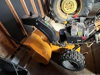 Front view of yellow Brute snow blower showing clearing housing, chute and right wheel