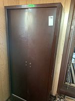 Full view of the tall brown metal cabinet with two doors closed, located against a wall.