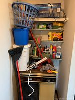 Overview of the cleaning supplies shelf showing laundry basket, broom, mop, cleaning bucket, assorted cleaning products and cloths.