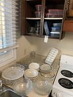 Overview of ceramic dishes, clear glass bowls, drinking glasses, and food storage containers on countertop and cabinet shelves.