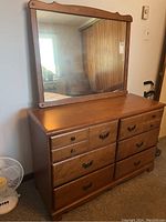 Front view of wooden dresser with attached mirror showing nine drawers; metal handles visible, warm brown finish.