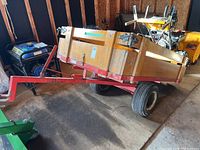 Side view showing red metal frame, wooden side panels, two wheels and tow hitch