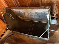 Top view of grass catcher attachment showing metal frame and black fabric bag with green rope handle.