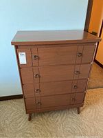Full front view of retro wooden highboy dresser showing four drawers and metal ring pulls, slight wear visible on veneer.