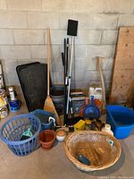 Full view of assorted household items including laundry basket, brooms, boot mats, dustpans, baskets, axe, paintbrushes, and buckets.