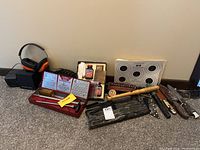 Wide shot of hunting tools including hearing protection, target practice sheets, knives, bottle oil, and wooden tools.