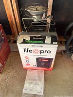 Front view of the Life Corp LifePro medium room infrared heater in its original box with owner's manual visible.