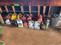 Multiple red and yellow jerry cans lined up with various car oil containers in front of a wooden wall.