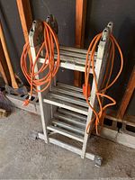 Front view of folded aluminum multi-position ladder with orange extension cords wrapped around it.