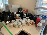 Full view of assortment on kitchen countertop including coffee makers, mugs, microwave, toaster, kettle.