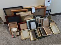 Wide shot showing a wide assortment of picture frames in various sizes and finishes, stacked against a wall on carpeted floor.