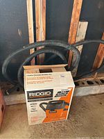 Photo of the Ridgid wet/dry vac setup with hose coiled around and the box in garage setting