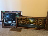 Photo of both velvet paintings together. One shows nighttime deer scene, the other daytime river scene.