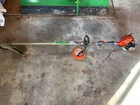 Full view of the Echo SRM-225 gas whipper snipper laid on the ground showing the full length with cutting head, shaft, and engine unit. Extra wire spool attached beside handle.