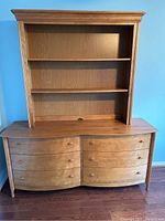 Overall view of vintage solid wood dresser with curved drawer fronts and matching hutch on a wood floor against blue wall
