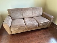 Front view of a beige taupe microsuede three-seat couch with plush cushions and rounded arms placed against a wall on wooden floor