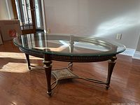 Oval glass coffee table with decorative perforated metal frame and legs on wood floor, show side view and top glass surface.