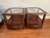Front view of two wood side tables with glass tops showing drawer and shelf storage