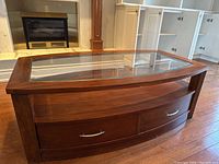 Front view of the rectangular wood coffee table with glass inset top, two drawers, and lower shelf on wood flooring.