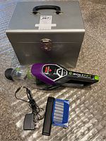 Metal storage box closed with Bissell BOLT PET 16V hand vacuum and accessories placed in front on the floor.