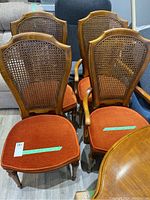 Front view of six wood dining chairs with cane backs and orange cushions, two with arms and four without.