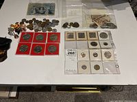 Overview of entire collection including coins, pins, banknote and vial on white surface