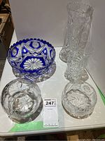 Top view of all five items on a white surface showing blue and clear crystal bowls and vases with cut glass patterns.