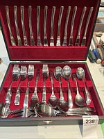 Open velvet lined box showing 12 knives aligned with handles up in top section and forks and spoons arranged in bottom section.