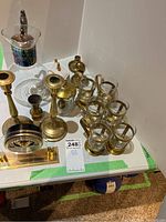 Photo of glass mugs, brass candlesticks, glass decanter, and clock arranged on table with green tape.