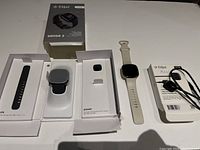 Opened Fitbit Sense 2 box showing packaging tray, black strap, charging puck and power adapter