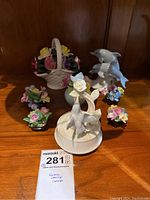 Lot displayed on a wooden shelf including hummingbird music box, ceramic dolphin figurines, and small floral decor pieces.