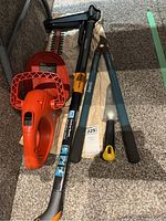 Photo showing orange and black Black & Decker hedge trimmer, Fiskars stand up weeder tool, blue handled garden loppers, and yellow and black handled garden saw.