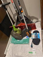 Overview photo showing the assembled gardening tools including two trimmers, rake, shovel, tarp and hose, arranged on white cloth.