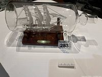 Front angled view showcasing the glass ship inside the transparent bottle with wooden base and engraved plaque.