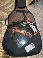 Soft guitar case on floor with guitar lesson book on top