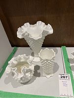 Set of three Fenton milk glass hobnail vases displayed together on a white surface with a brown background. The vases vary in shape and size, two with ruffled tops and one with hexagonal scalloped edges.