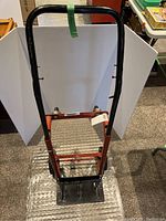 Full view of moving dolly standing upright showing red frame, black handle, and loading platform.