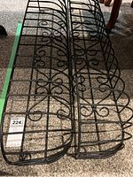 Two black metal garden plant holders side by side, showing scrollwork decoration and grid base.