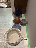 Wide shot showing all six pottery pieces on white surface including large white crock and smaller lidded containers