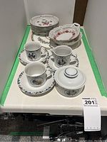 Overview photo showing 6 plates, cups, saucers, milk jug, sugar bowl arranged on a white shelf.
